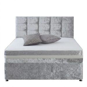 Grijs fluwelen divanbed met panelen hoofdbord, matras en twee grijze sierkussens van voren